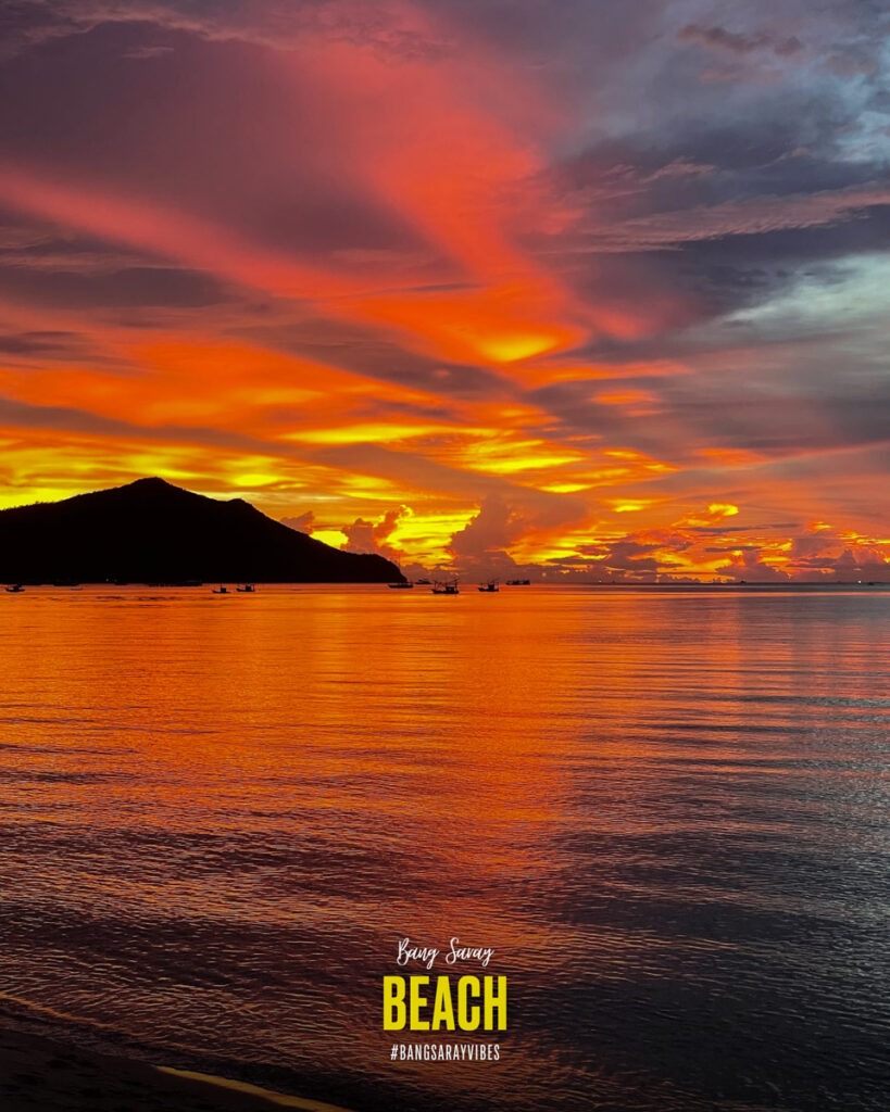 The picture shows a sunset over the water at Bang Saray Beach, capturing the tranquil beauty of nature as the sun sets on the horizon, painting the evening sky red.